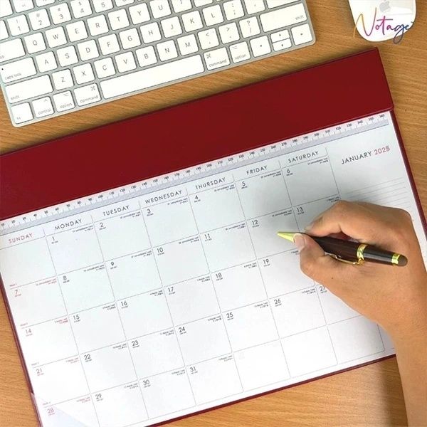 Hand skriver i en öppen månads kalender bredvid ett tangentbord