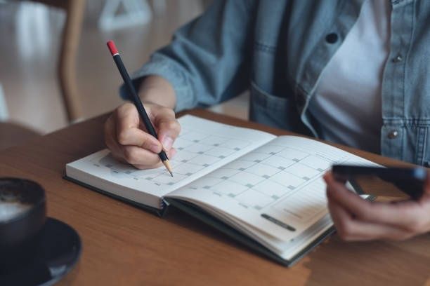 Person skriver i en kalender medan en mobiltelefon hålls i handen