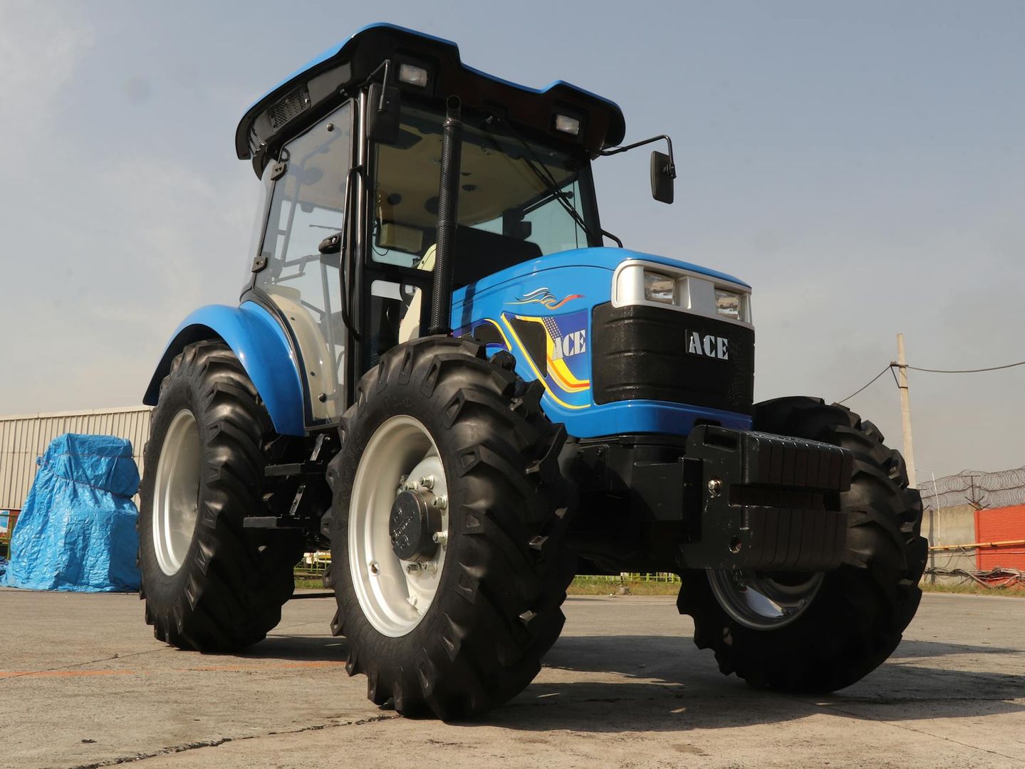 En modern blå ACE-traktor parkerad på en asfalterad yta under en klar himmel.