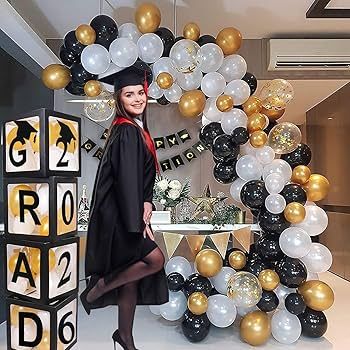 En student i kåpa framför en ballongbåge och dekorativa boxar.